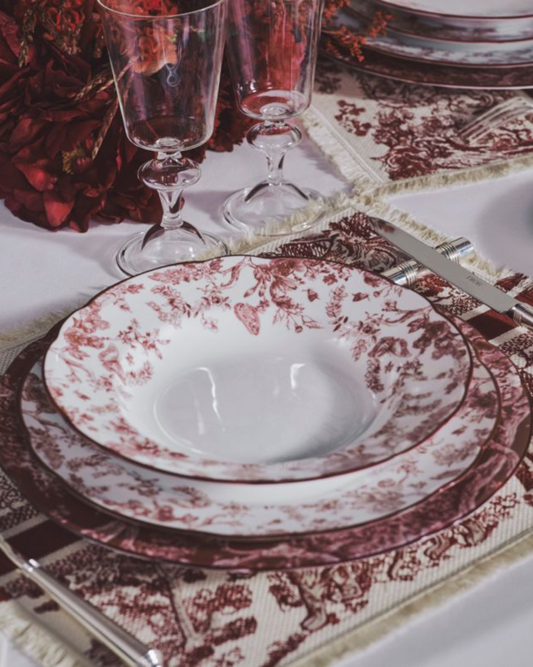 Table élégamment dressée avec de la vaisselle fine à motifs rouges et verres en cristal sur une nappe assortie