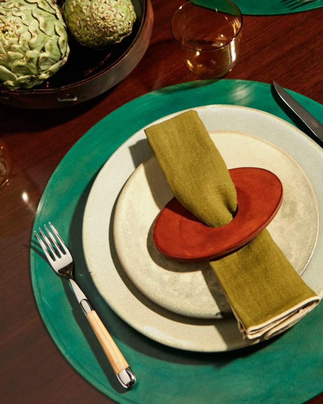 Assiette raffinée sur un grand sous-plat vert, avec une serviette verte maintenue par un rond de serviette en bois rouge