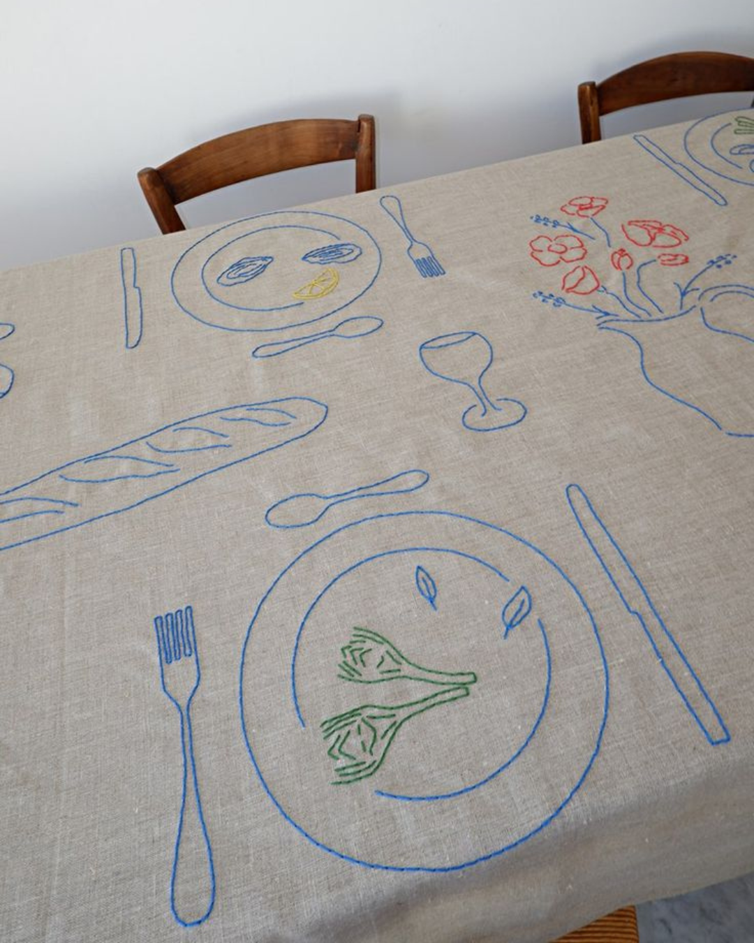 Nappe beige brodée de motifs d'artichauts, baguettes et verres, dressée sur une table en bois rustique