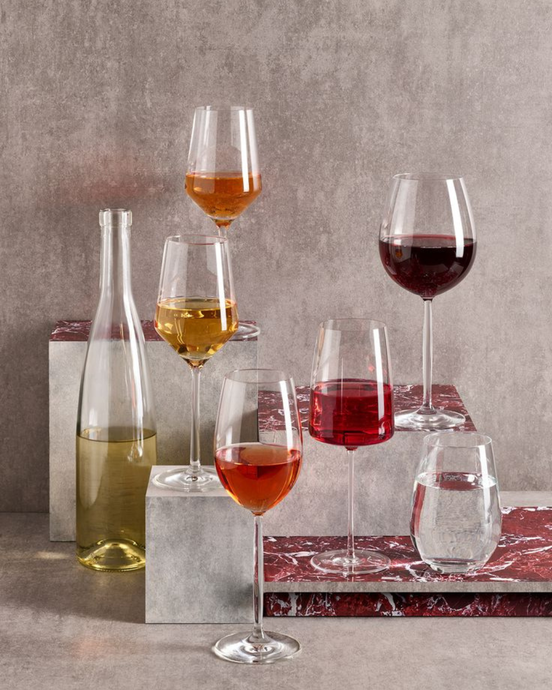 Sélection de verres à vin colorés, disposés sur des blocs en marbre rouge et gris pour une présentation design